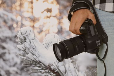 Professional photographer with modern camera and blurred view of snowy forest, space for text