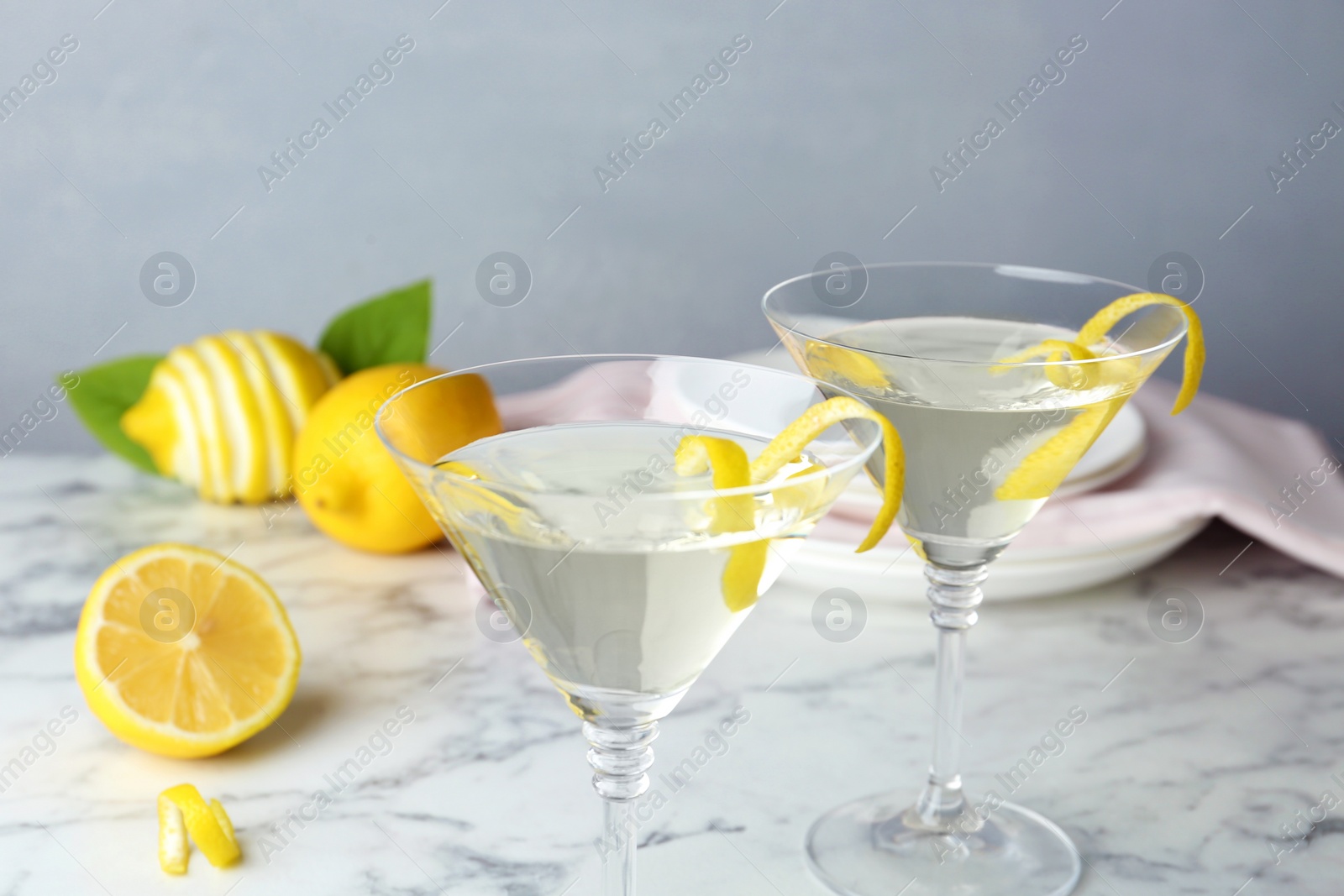 Photo of Glasses of lemon drop martini cocktail with zest on marble table against grey background