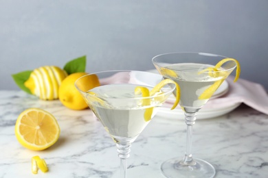 Photo of Glasses of lemon drop martini cocktail with zest on marble table against grey background