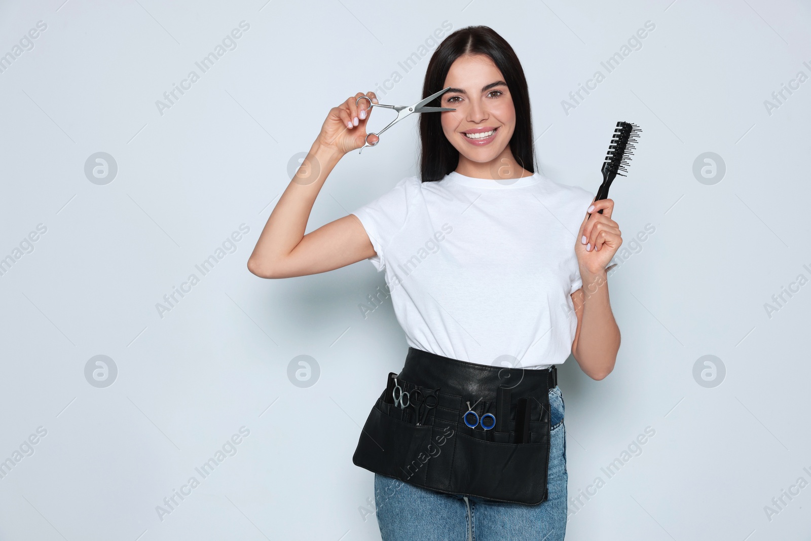 Photo of Portrait of happy hairdresser with professional scissors and vent brush on light background