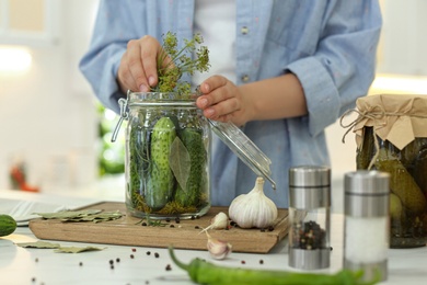 Photo of Woman putting dill into pickling jar at table in kitchen, closeup