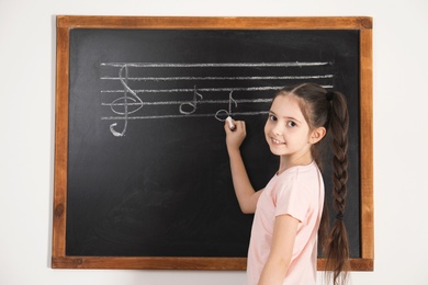 Photo of Little girl writing music notes on blackboard in classroom