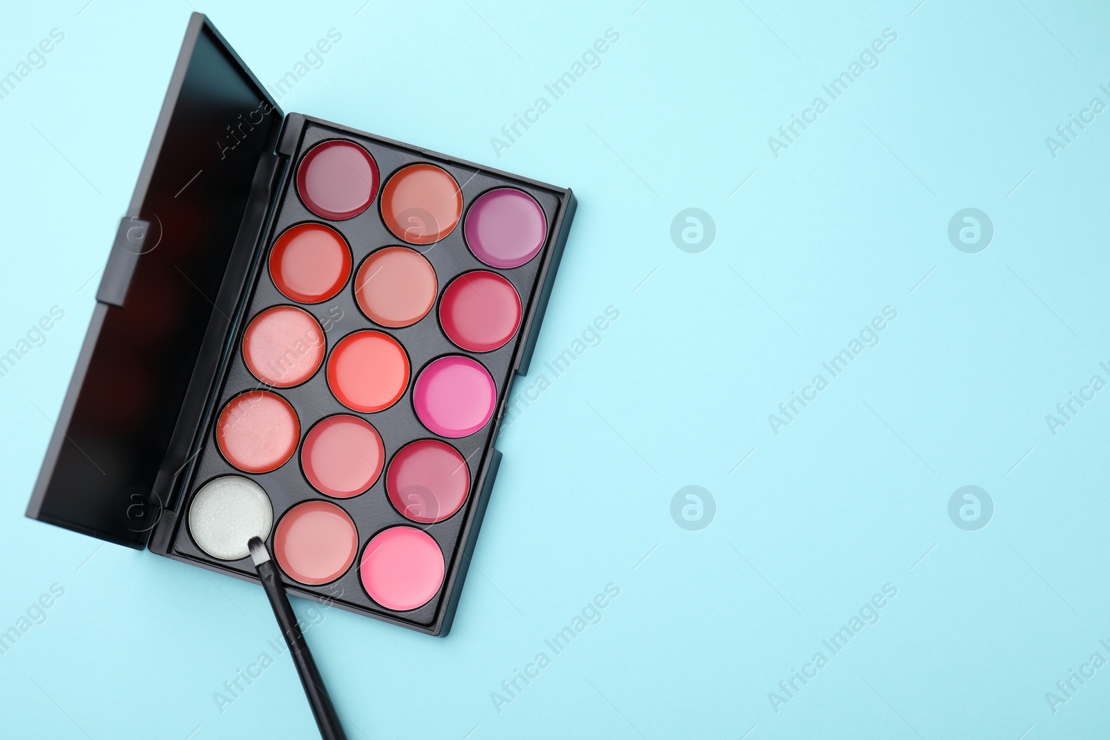 Photo of Cream lipstick palette and brush on light turquoise background, flat lay with space for text. Professional cosmetic product
