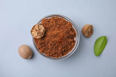 Nutmeg powder in bowl, seeds and green leaf on white background, flat lay