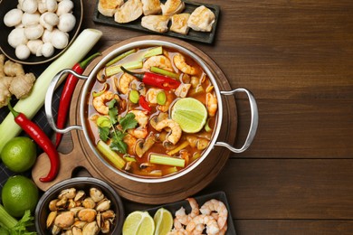 Saucepan with delicious Tom Yum soup and ingredients on wooden table, flat lay. Space for text