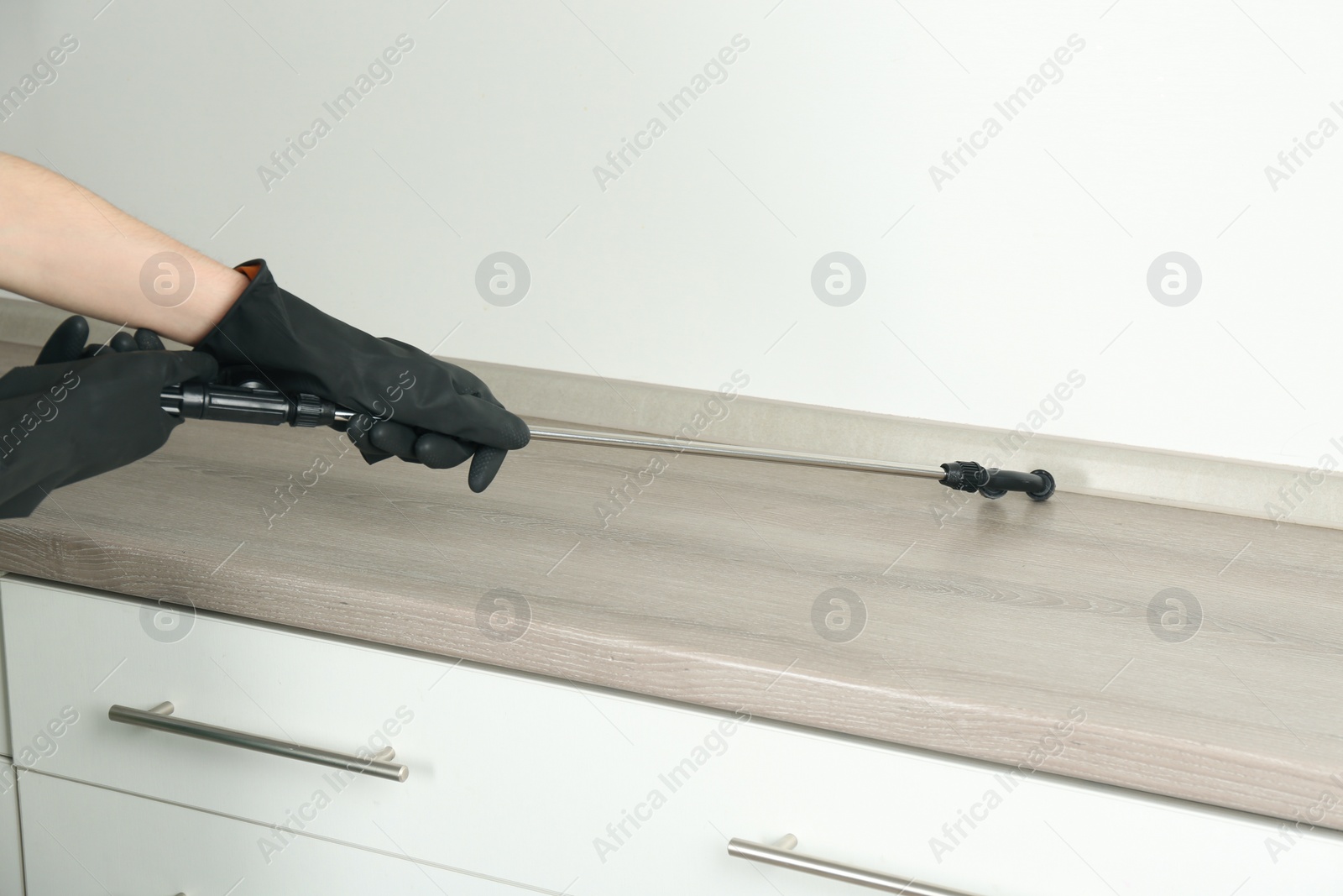 Photo of Pest control worker spraying pesticide on furniture indoors, closeup