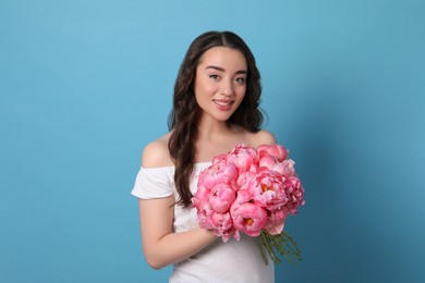 Photo of Beautiful young woman with bouquet of pink peonies on light blue background