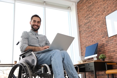 Photo of Portrait of young man in wheelchair with laptop at office
