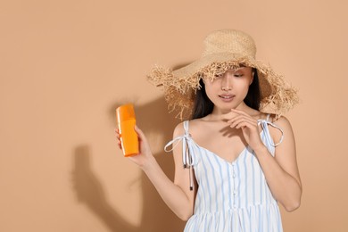 Photo of Beautiful young woman in straw hat holding sun protection cream on beige background, space for text