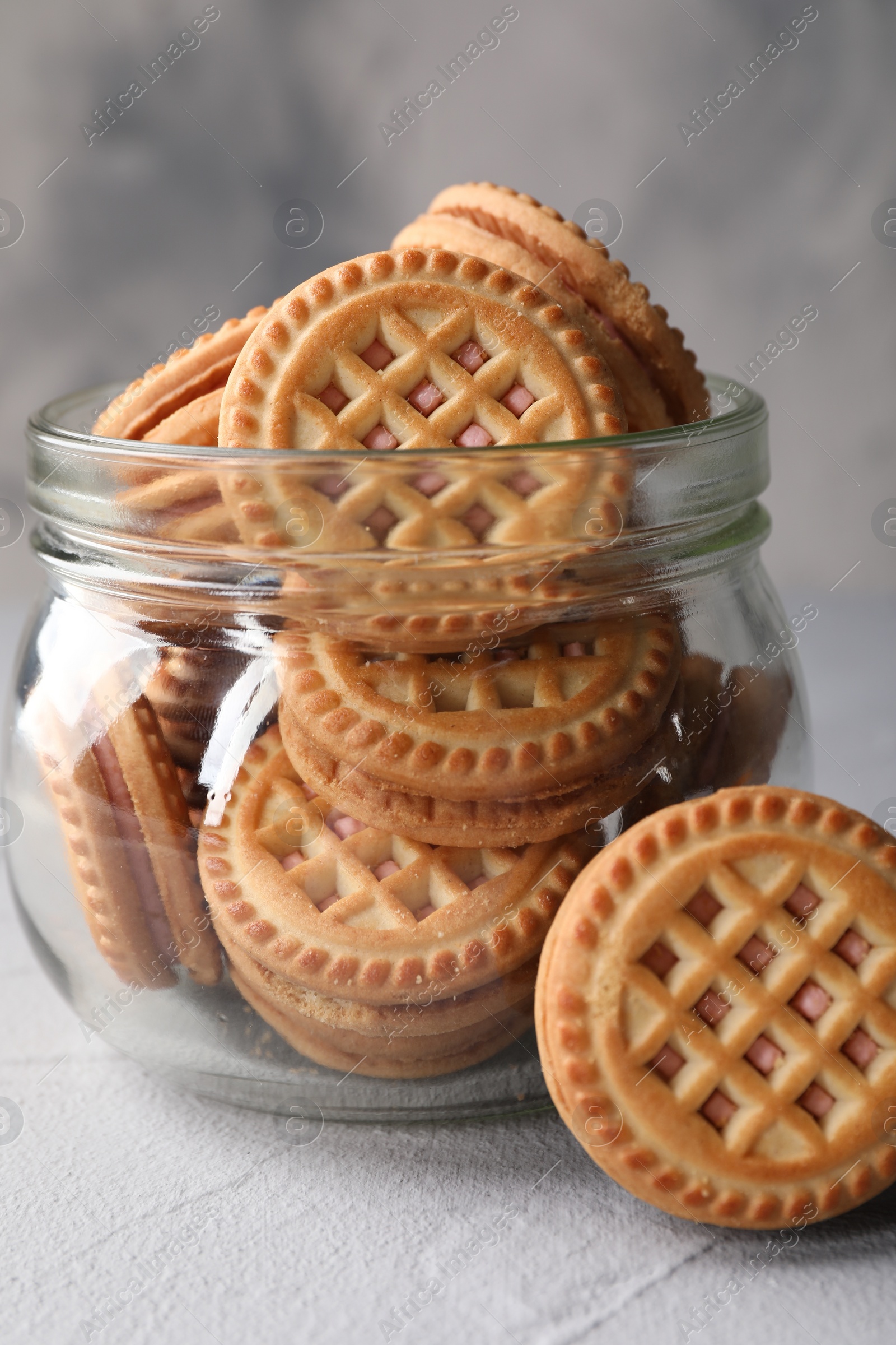 Photo of Tasty sandwich cookies with cream in jar on light grey table, closeup