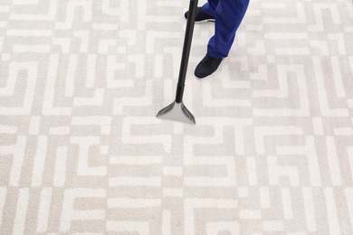 Man removing dirt from carpet with vacuum cleaner indoors, closeup. Space for text