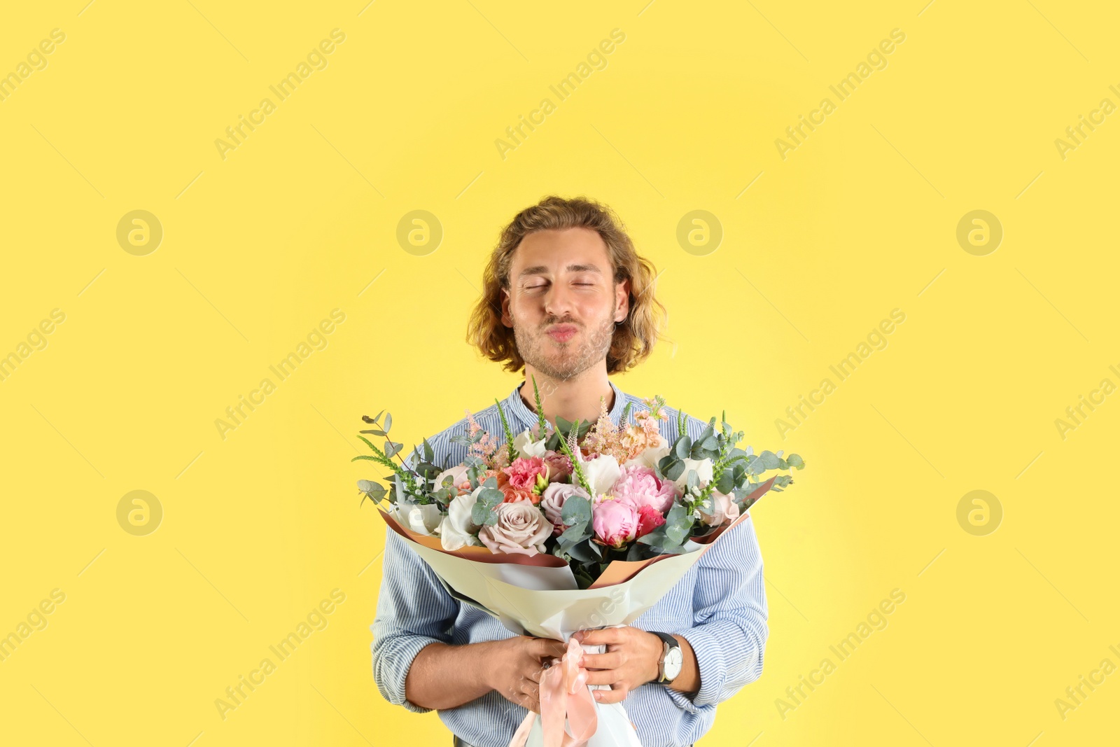 Photo of Young handsome man with beautiful flower bouquet on yellow background