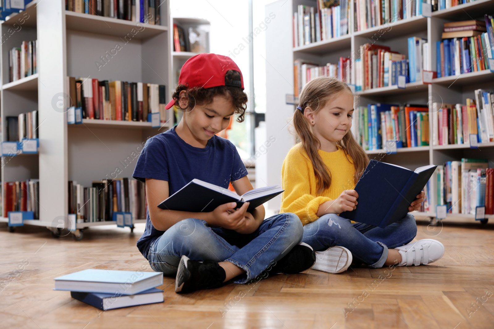 Photo of Cute little children reading books on floor in library