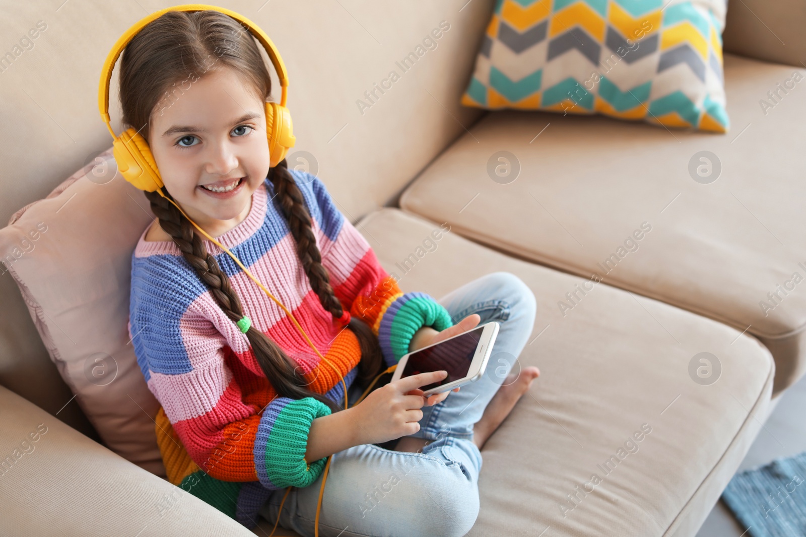 Photo of Cute child with headphones and mobile phone on sofa indoors. Space for text