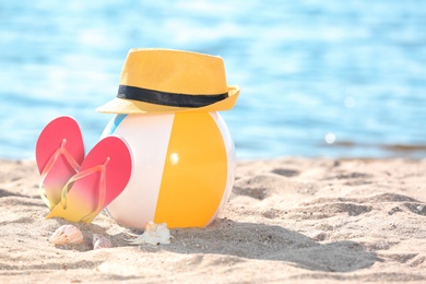 Photo of Inflatable ball, hat and flip flops on sand near sea. Beach object