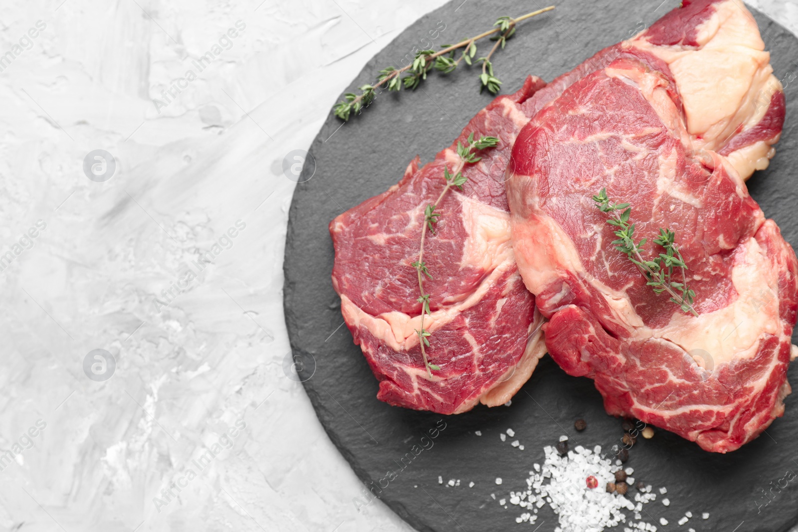 Photo of Fresh raw beef cut with different spices on light grey textured table, top view. Space for text