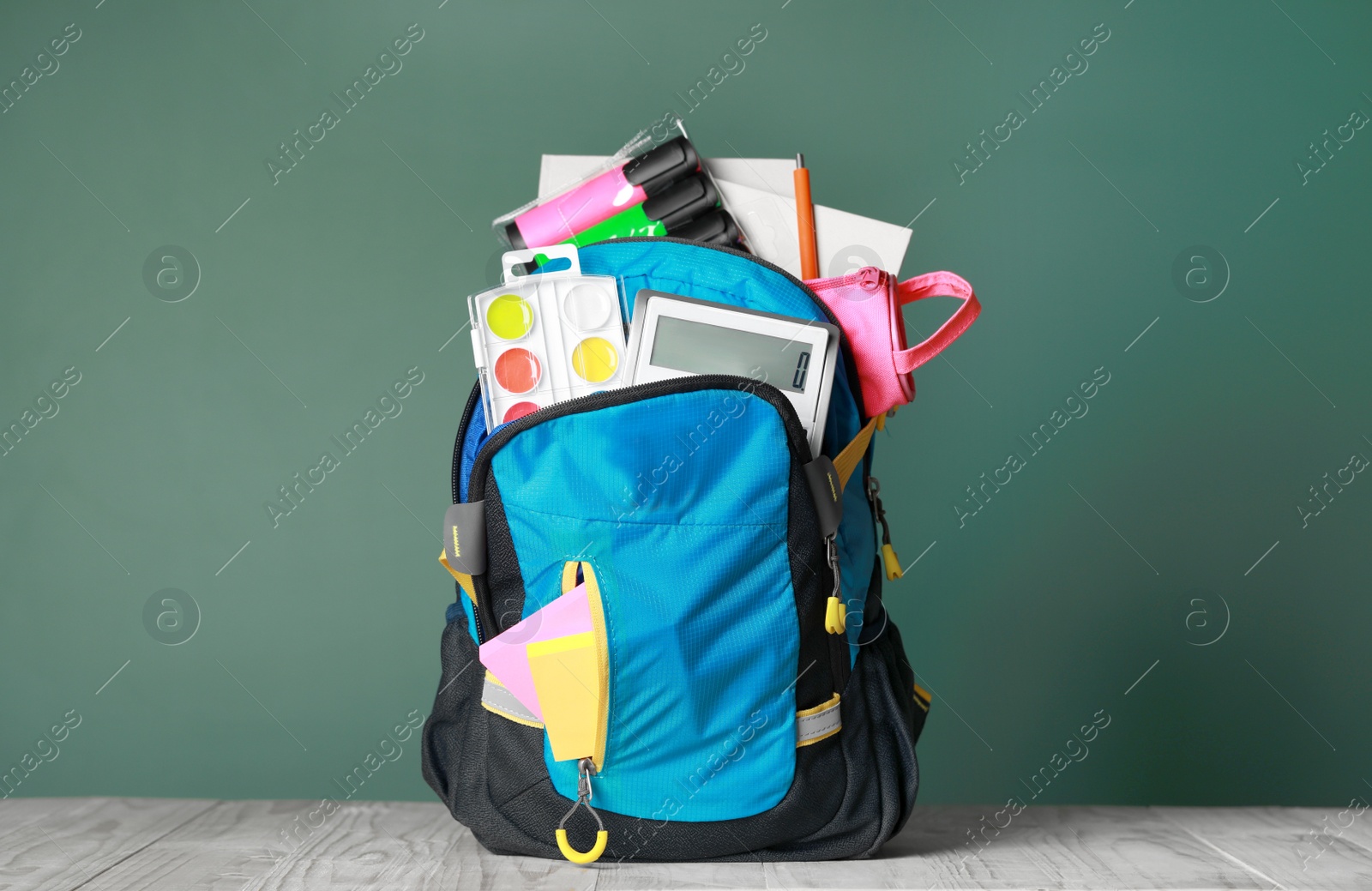 Photo of Backpack with different school stationery on white wooden table near chalkboard