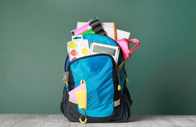 Photo of Backpack with different school stationery on white wooden table near chalkboard