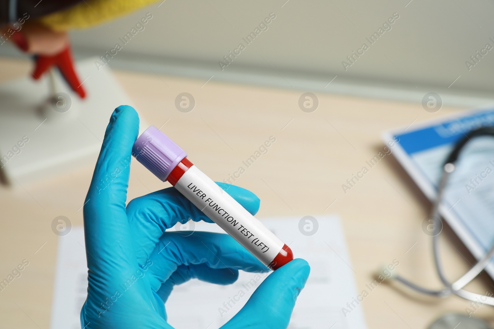 Photo of Laboratory worker holding tube with blood sample and label Liver Function Test over table, closeup