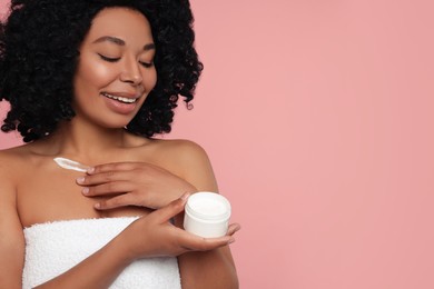 Photo of Young woman applying cream onto body on pink background. Space for text