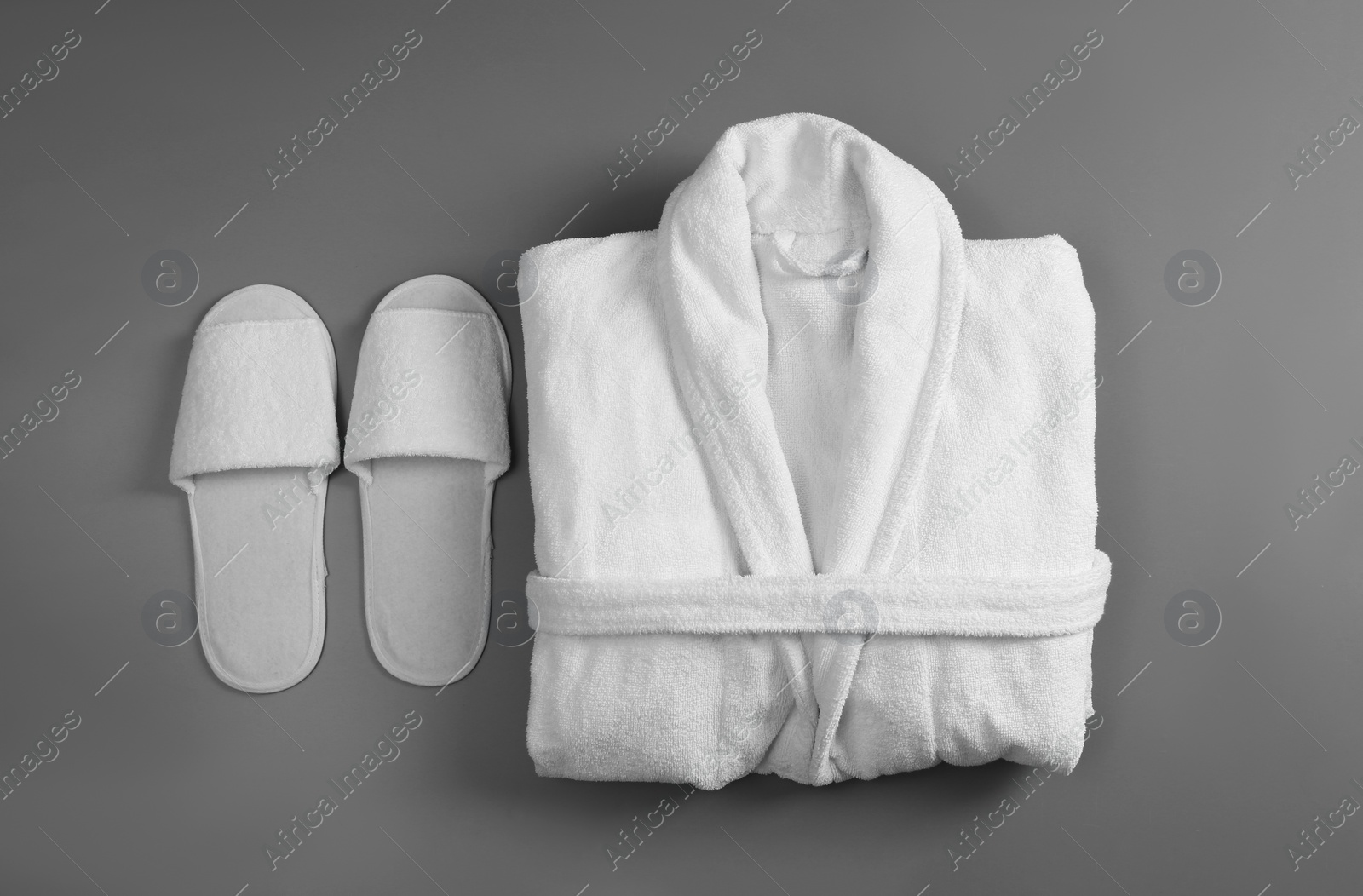 Photo of Clean folded bathrobe and slippers on grey background, flat lay