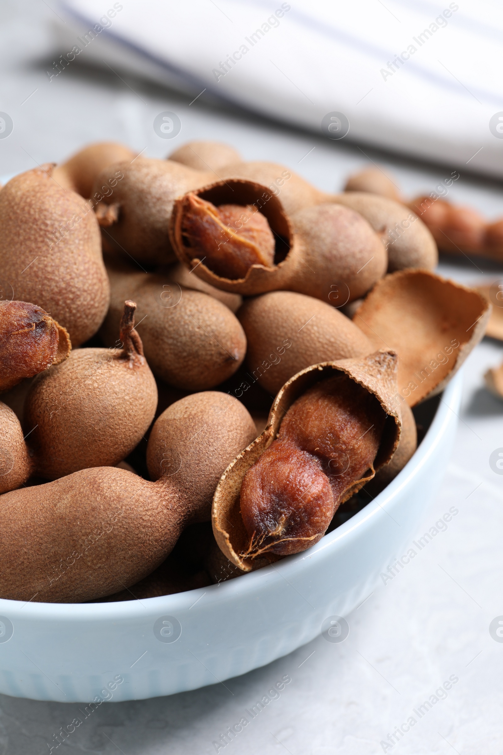 Photo of Delicious ripe tamarinds in ceramic bowl on table, closeup