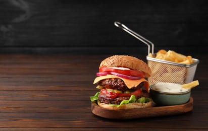 Tasty cheeseburger with patties, French fries and sauce on wooden table. Space for text