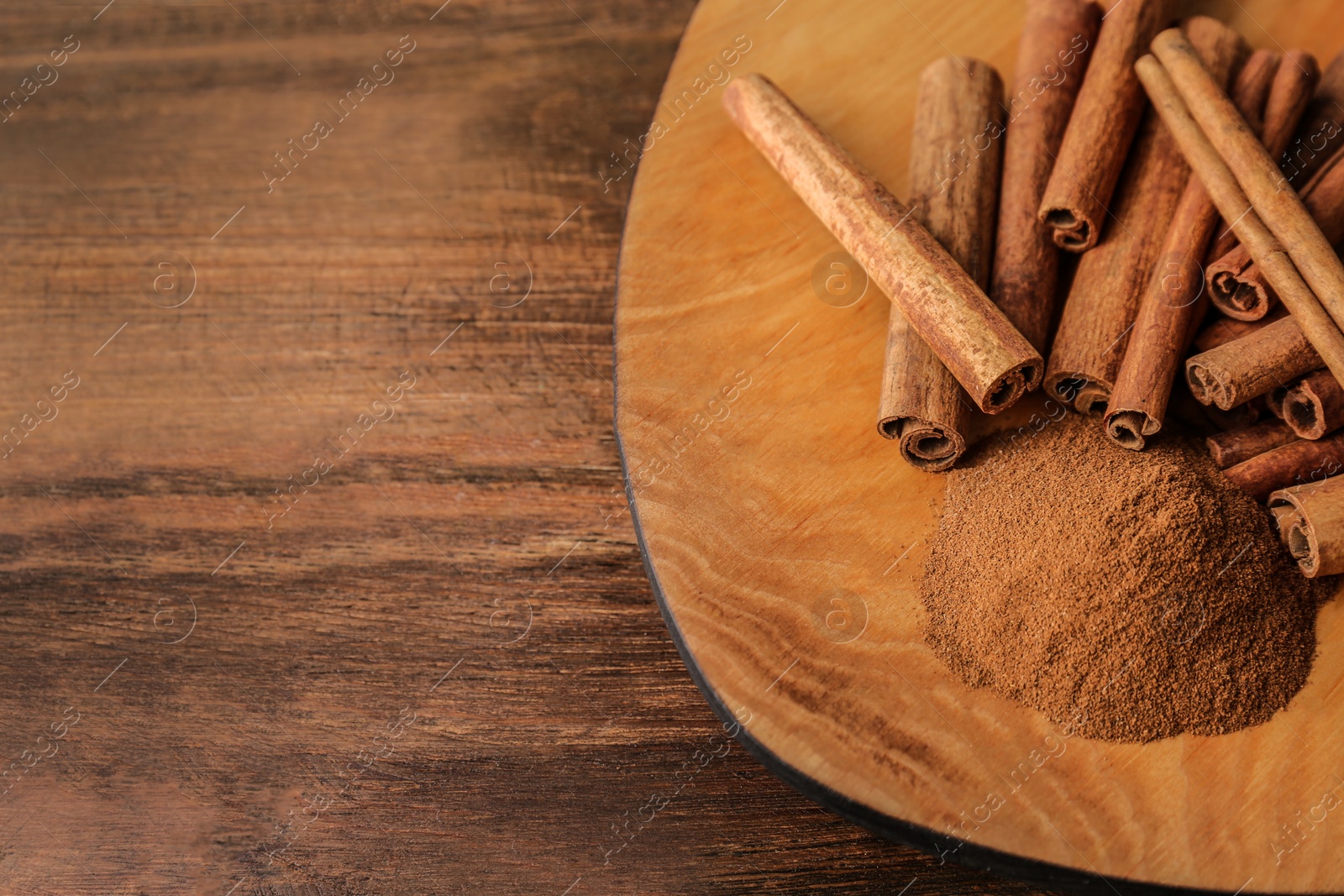 Photo of Plate with aromatic cinnamon powder and sticks on wooden table