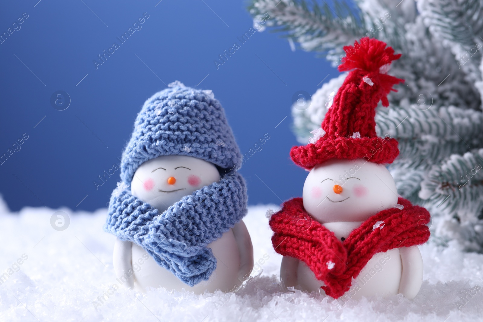 Photo of Cute decorative snowmen and fir tree on artificial snow against light blue background, closeup