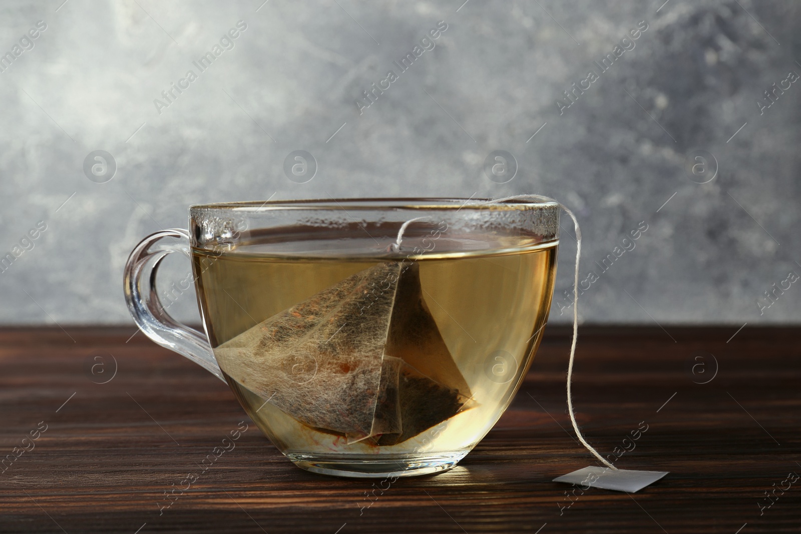 Photo of Tea bag in glass cup on wooden table, closeup