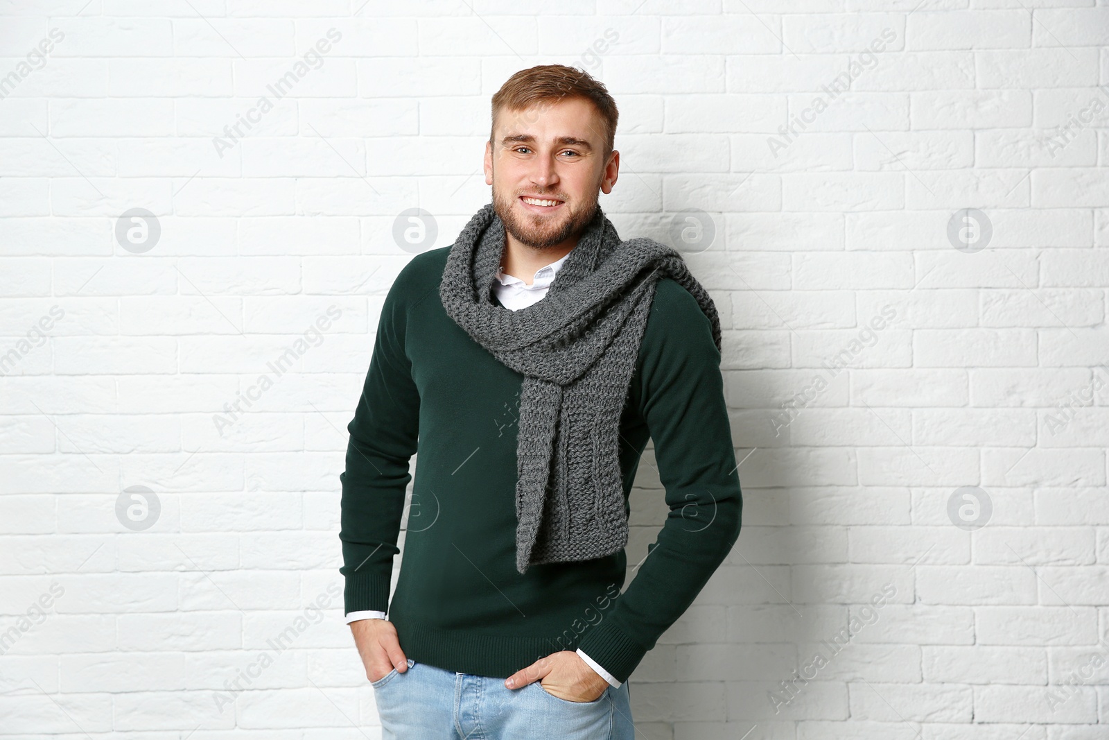 Photo of Handsome young man in warm sweater with scarf near white brick wall