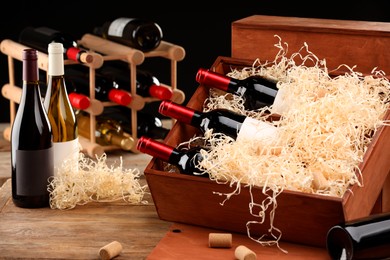 Box with wine bottles on wooden table against black background