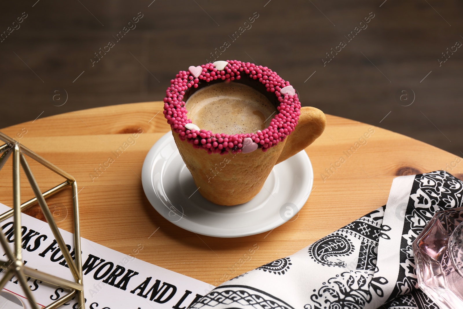 Photo of Delicious edible biscuit cup of coffee decorated with sprinkles on wooden table
