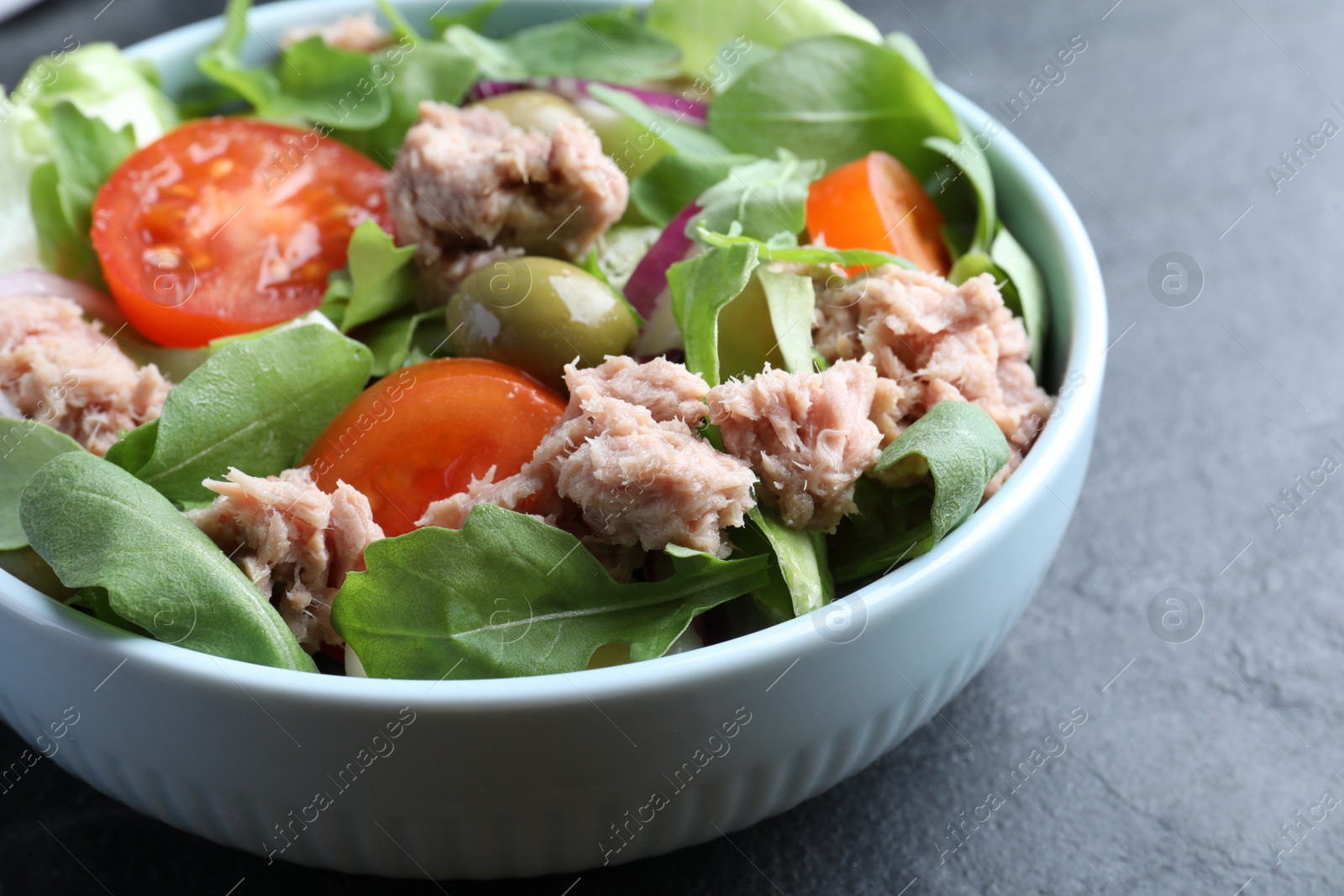 Photo of Bowl of delicious salad with canned tuna and vegetables on black table, closeup