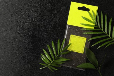 Scented sachet and green leaves with water drops on black table, flat lay. Space for text