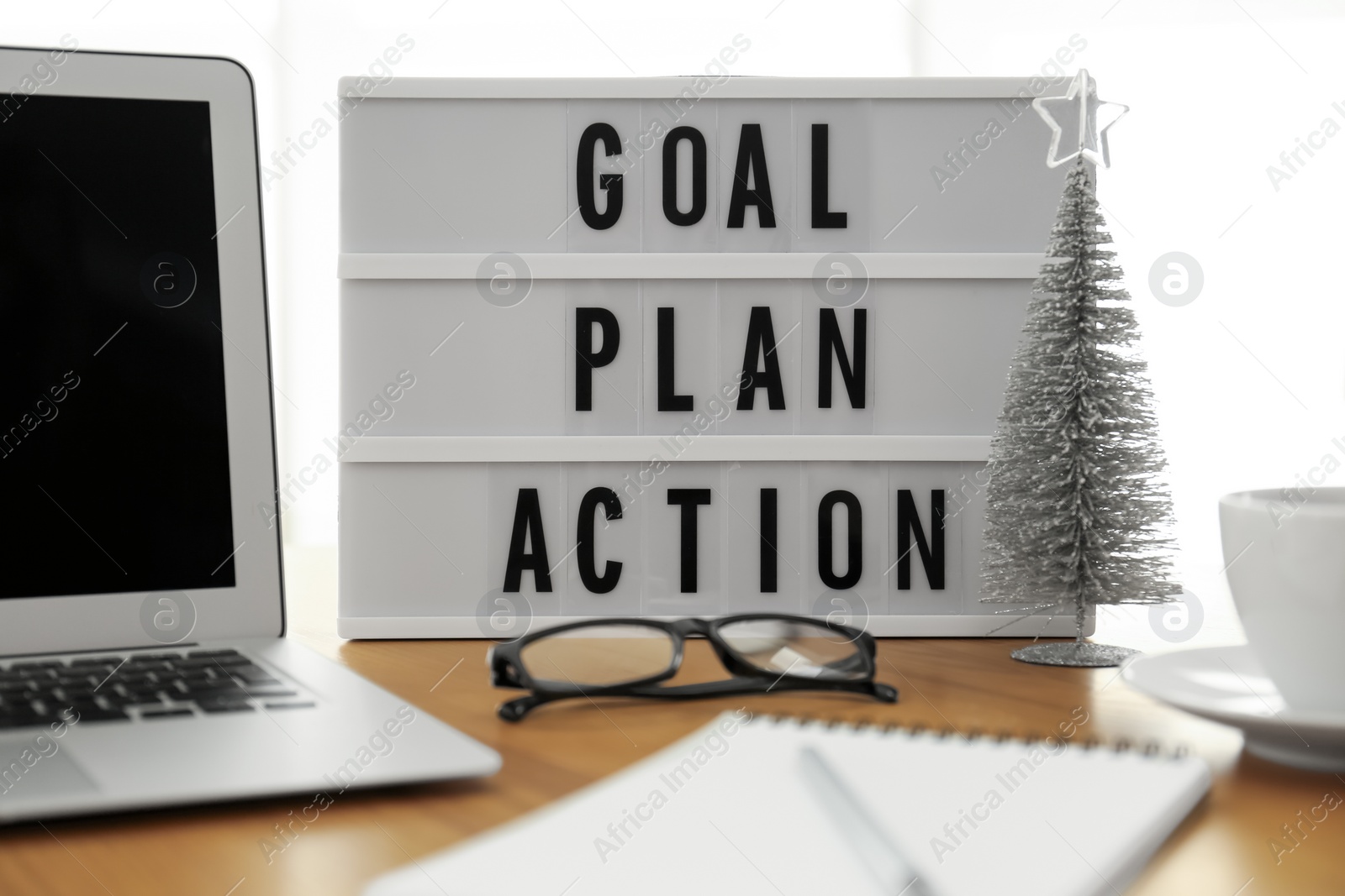 Photo of Light box with words Goal Plan Action near laptop on wooden table