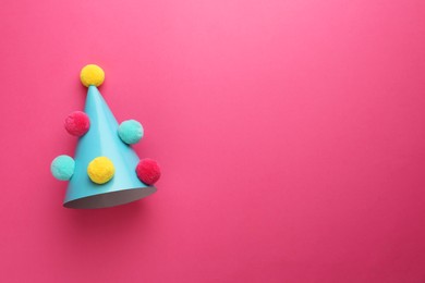 Photo of One light blue party hat with pompoms on pink background, top view. Space for text