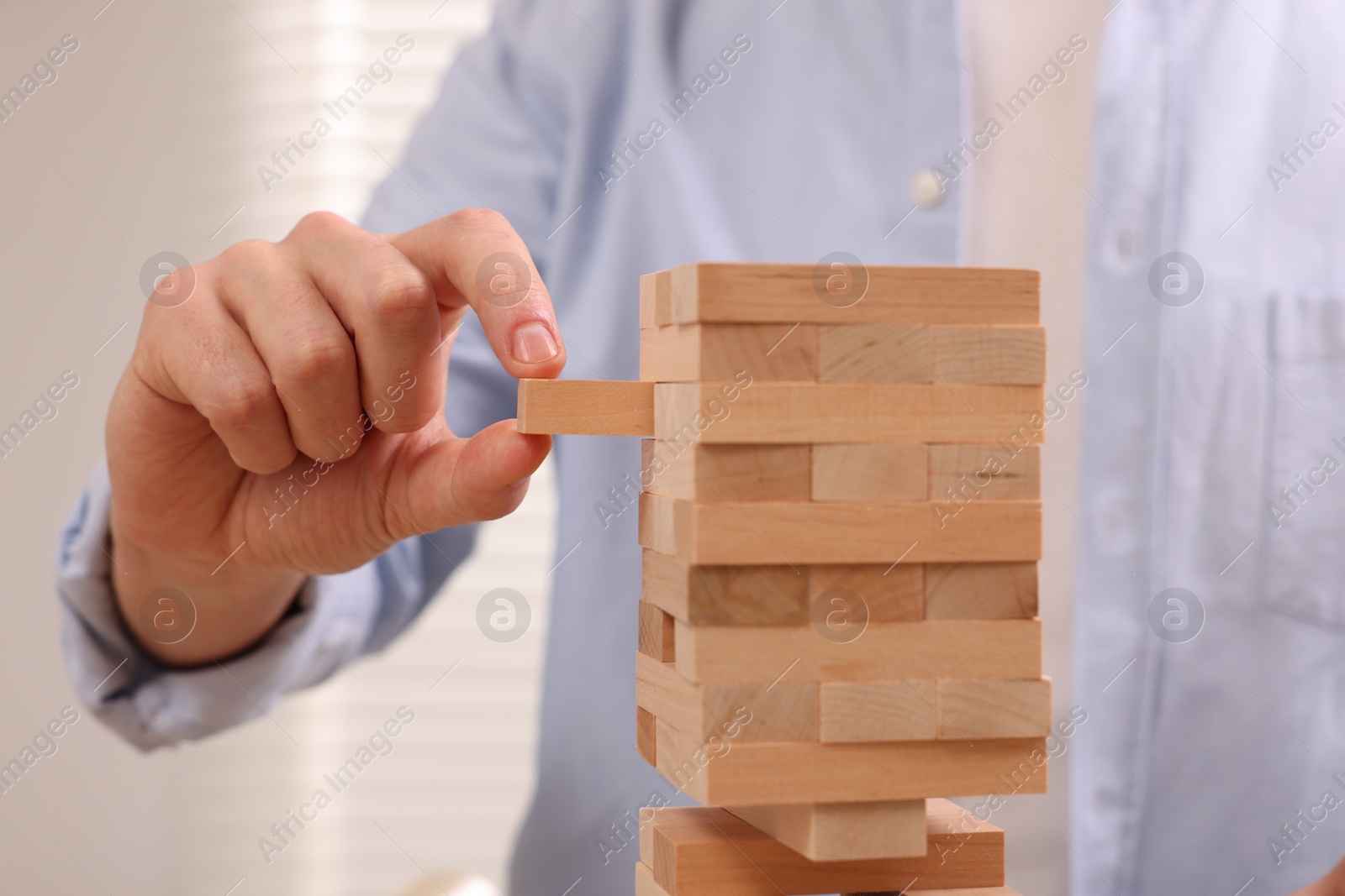 Photo of Playing Jenga. Man removing wooden block from tower indoors, closeup