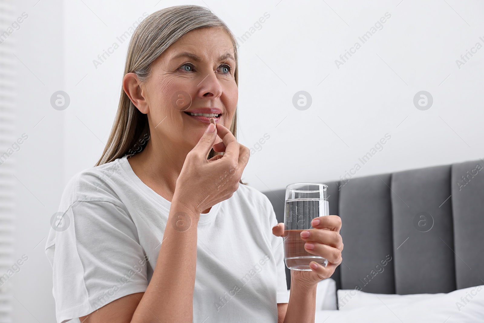 Photo of Beautiful woman taking vitamin pill in bedroom