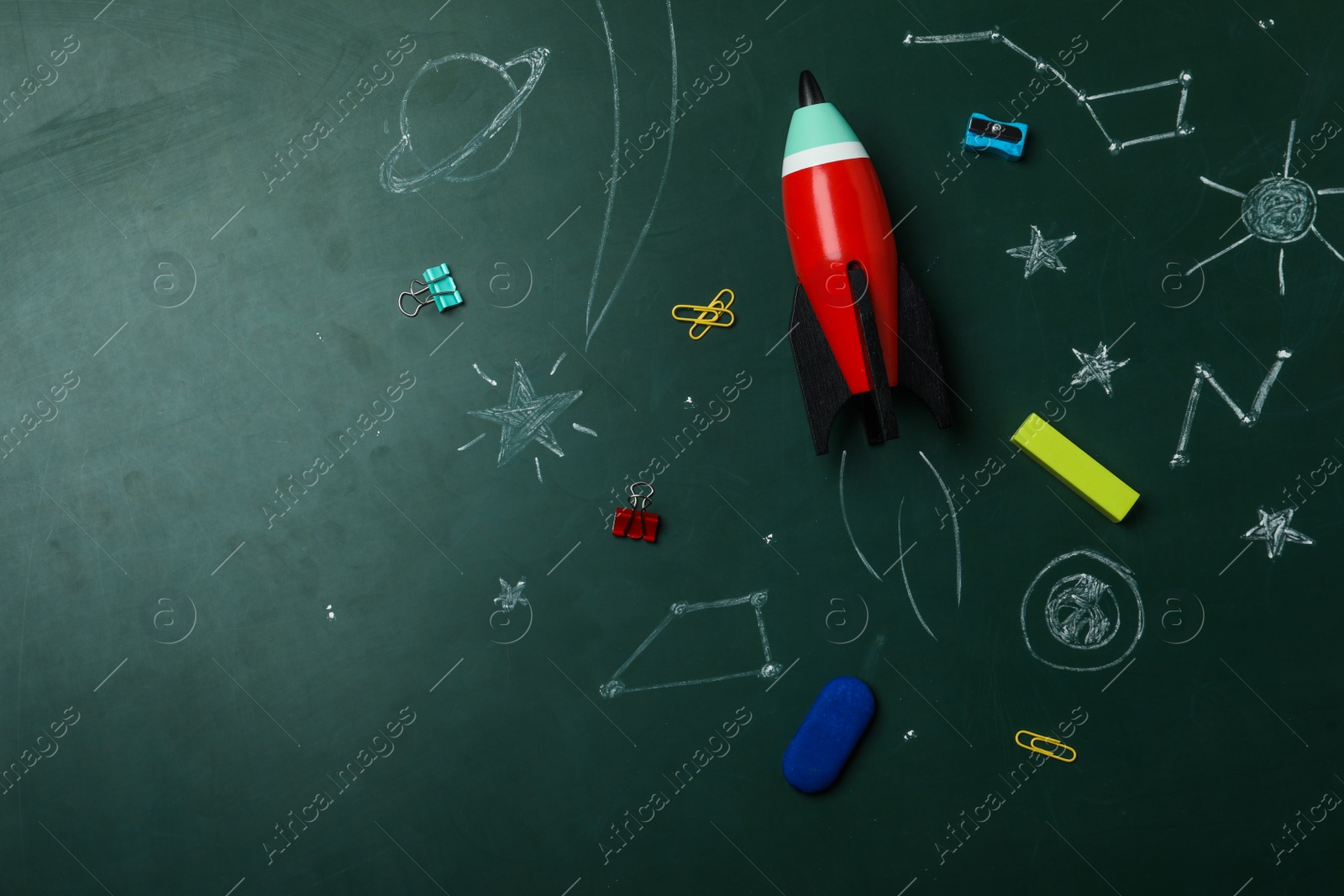 Photo of Bright toy rocket, school supplies and drawings on chalkboard, flat lay. Space for text