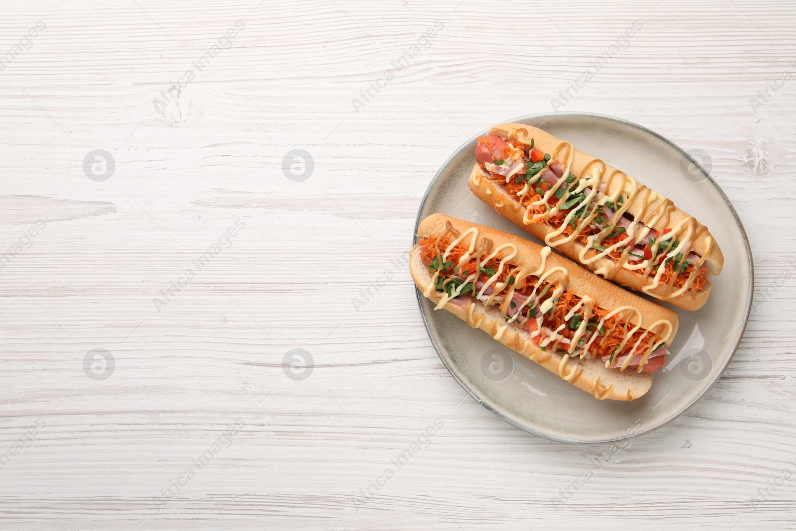 Photo of Delicious hot dogs with bacon, carrot and parsley on white wooden table, top view. Space for text