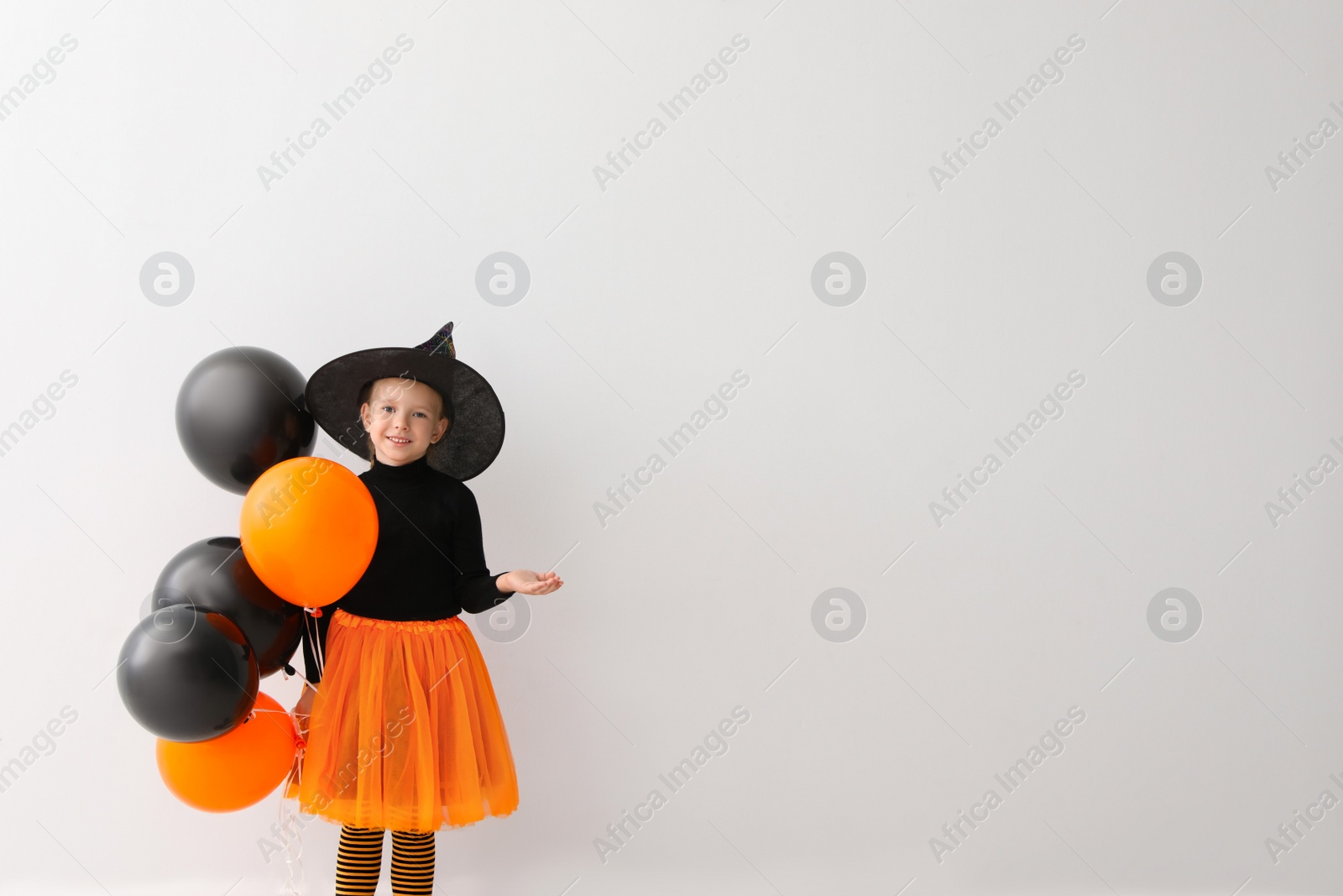 Photo of Cute little girl with balloons wearing Halloween costume on light background. Space for text
