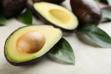 Whole and cut avocados with green leaves on light table, closeup