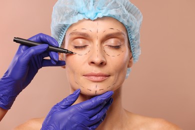 Doctor with marker preparing patient for cosmetic surgery operation on light brown background, closeup