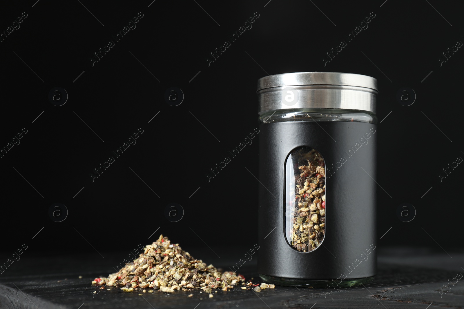 Photo of Stylish shaker with pepper on wooden board against black background, closeup. Space for text