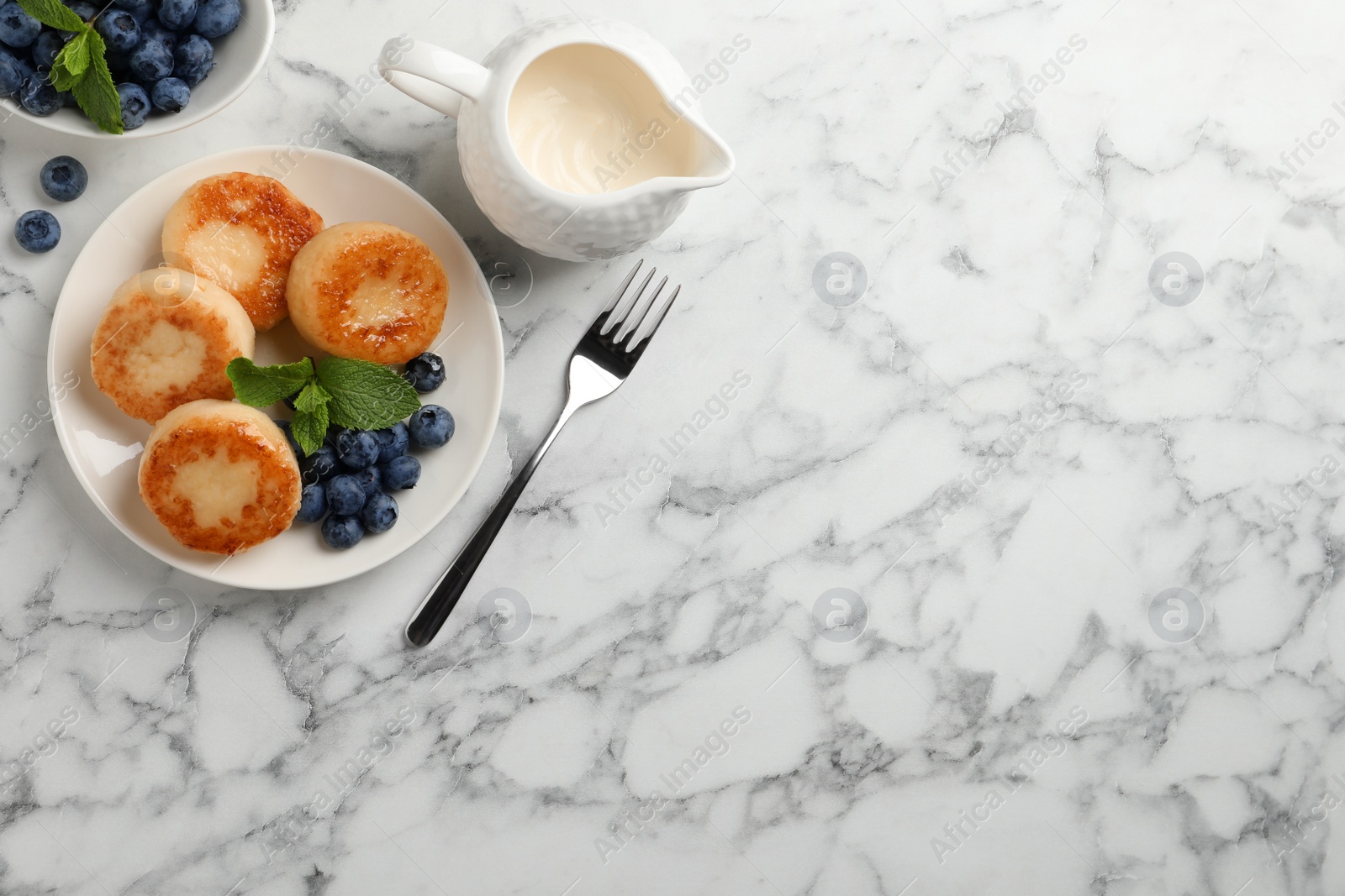 Photo of Delicious cottage cheese pancakes with blueberries, honey and mint on white marble table, flat lay. Space for text