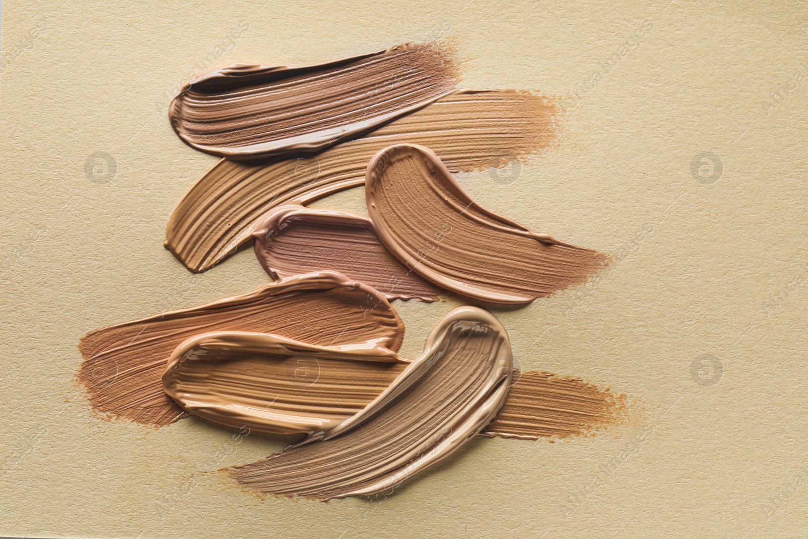 Image of Different shades of liquid foundation on beige background, top view