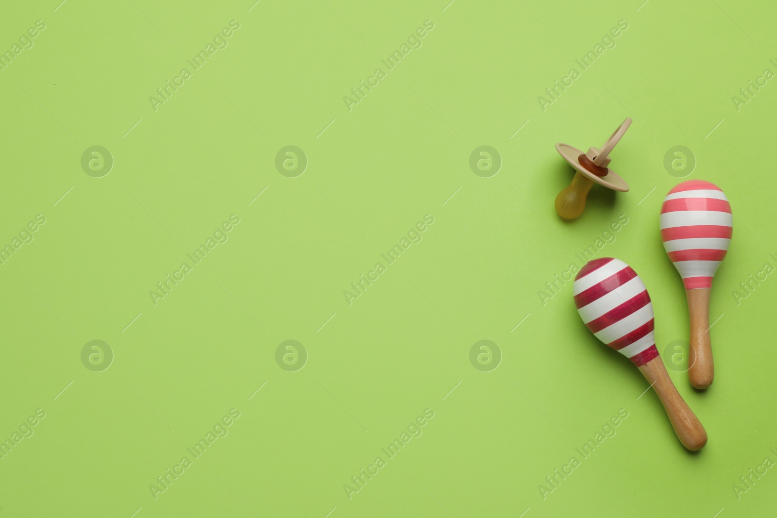 Photo of Wooden rattles and pacifier on light green background, flat lay. Space for text