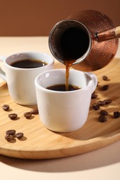 Pouring aromatic coffee from cezve into cup at table, closeup