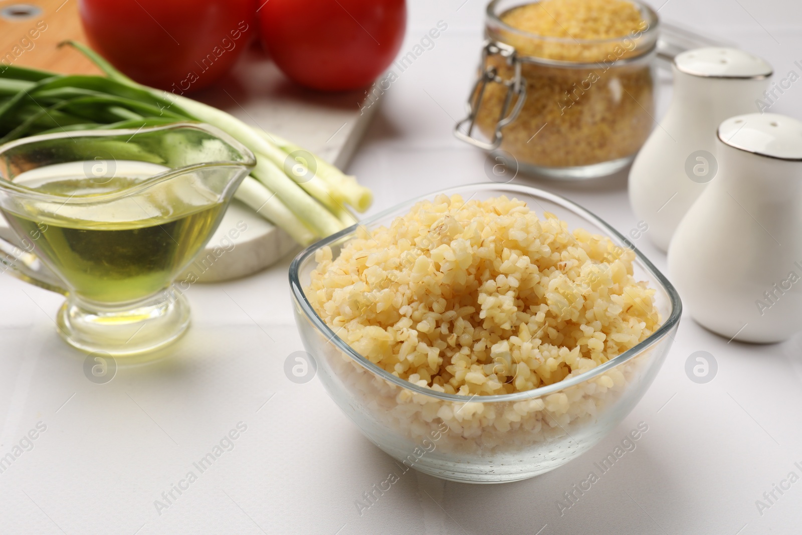 Photo of Delicious bulgur in bowl and products on white tiled table, closeup